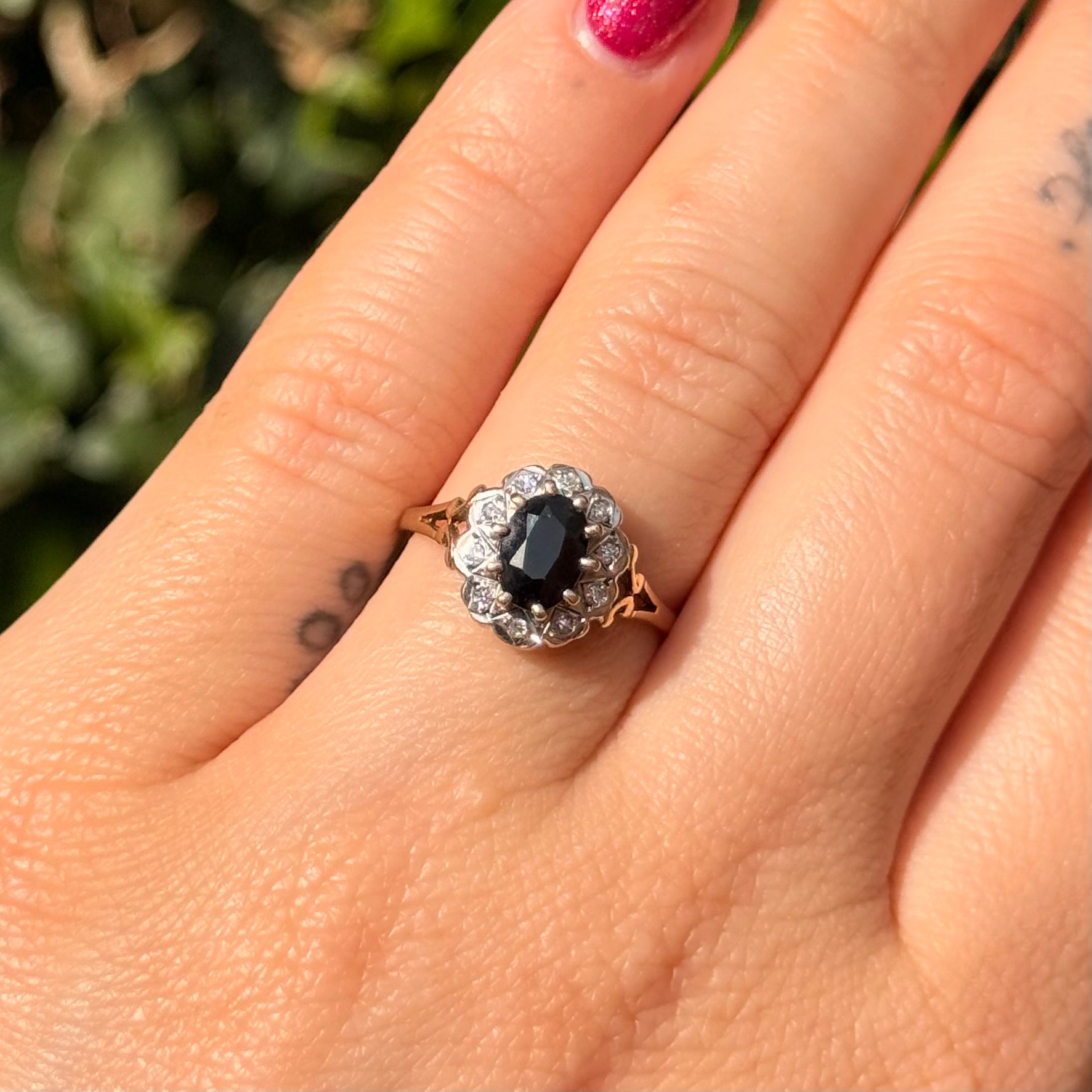 gold ring with a black gemstone on a person's finger against a blurred green background